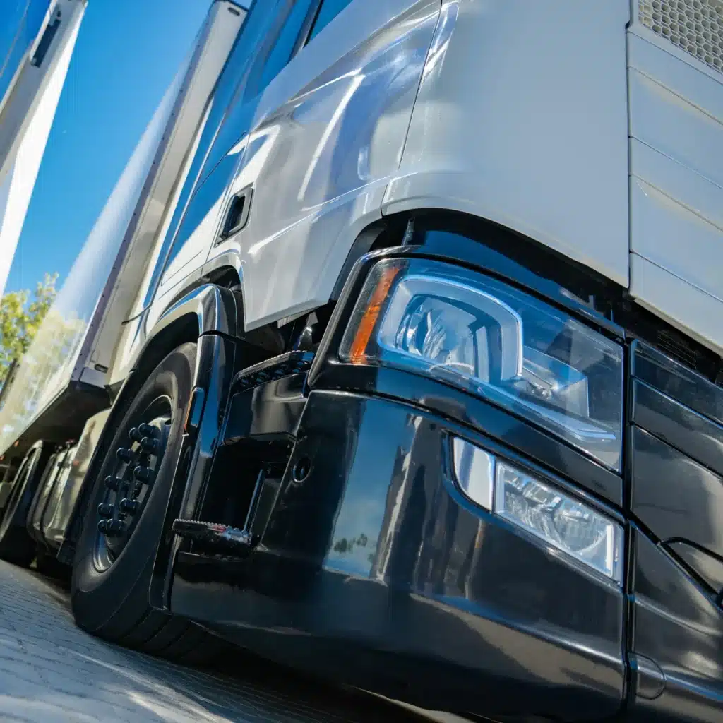 Camion blanc moderne : focus sur le design et la puissance Camion poids lourd blanc moderne en contre-plongée avec phare brillant, stationné sous un ciel bleu.